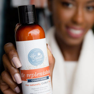 Woman smiling and holding tlc replenishing conditioner for naturally curly hair