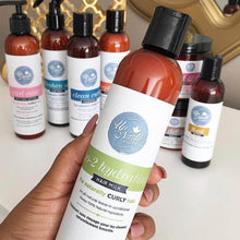 Load image into Gallery viewer, Woman holding go-2 hydrating hair milk for naturally curl hair in front of a gold trim mirror and other up north natural products in the background