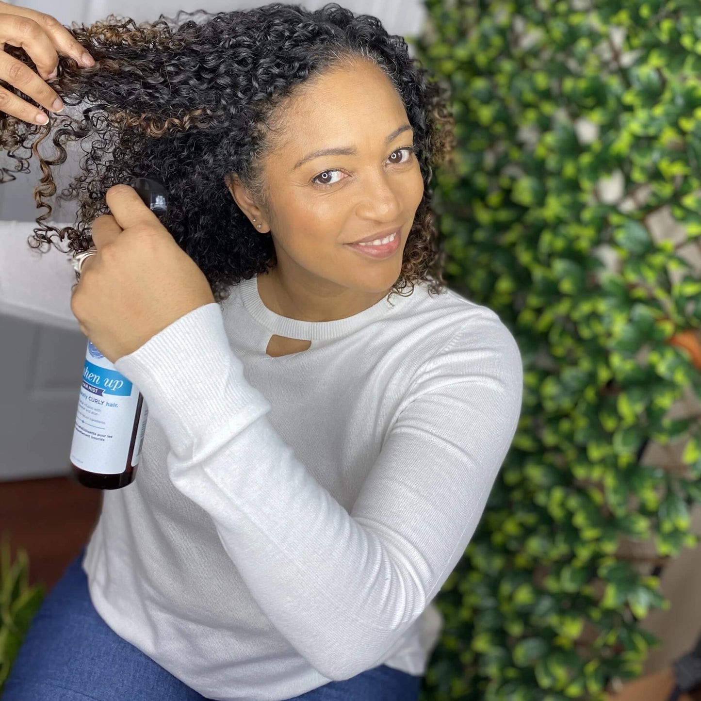 Women with naturally curly hair sectioning her hair and spraying freshen up hair mist